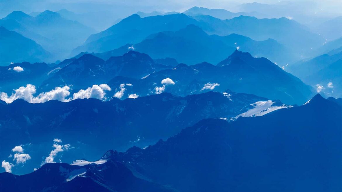 Vista aérea de una cadena montañosa con una luz azulada, las montañas más lejanas casi no se ven