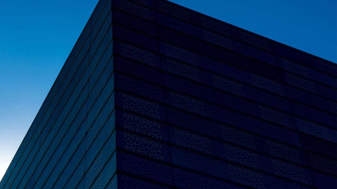La esquina superior de un edificio alto y de color oscuro, recortada contra un despejado cielo azul