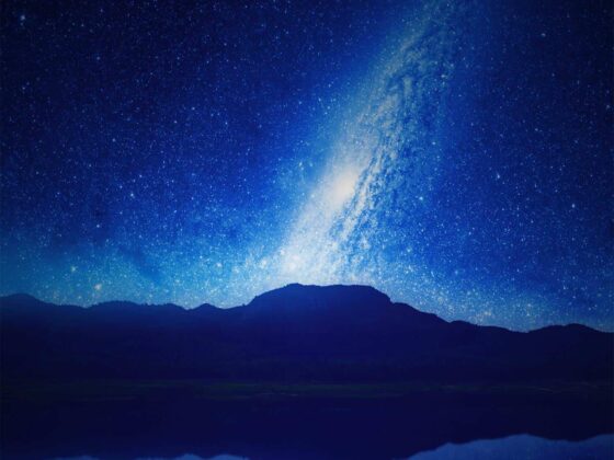 Vista nocturna de la Vía Láctea que parece elevarse dese una montaña y que se refleja en un lago