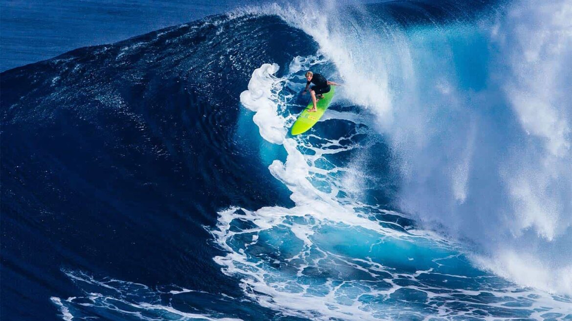 Un surfista con una tabla verde fosforito cabalga la parte final de una ola que rompe detrás de él