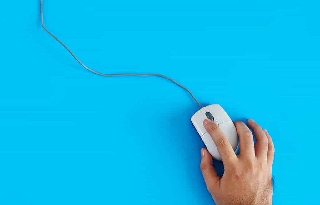 Un ratón blanco de cable, manejado con la mano derecha por una persona fuera de cuadro de la foto