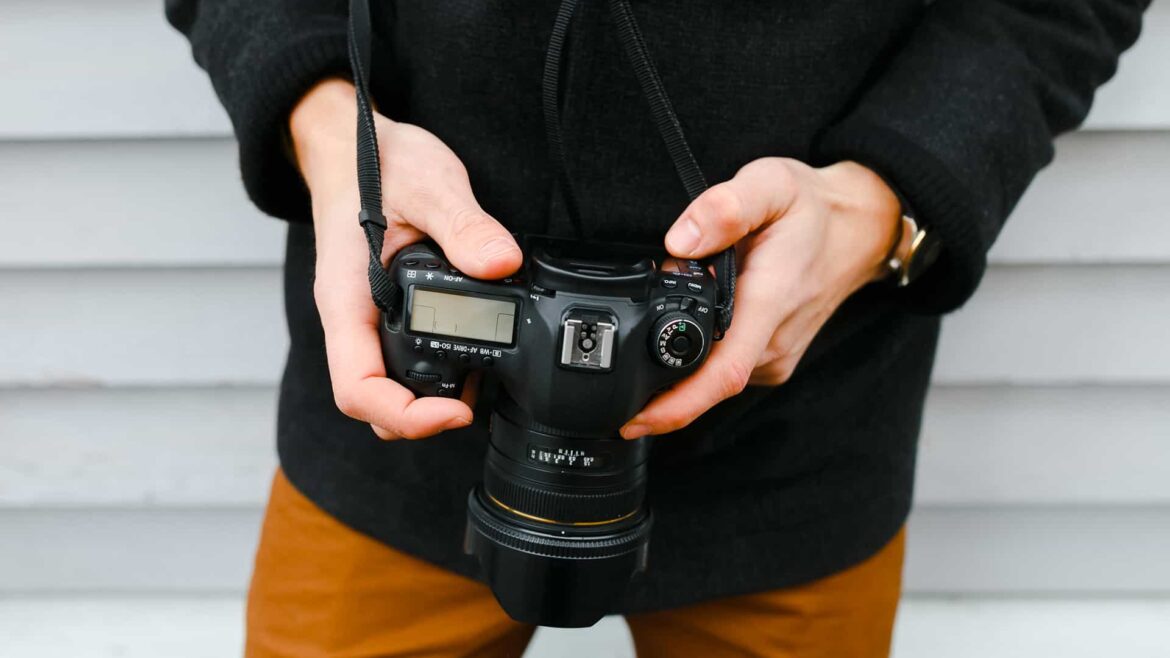 Una persona sujetando una cámara reflex digital apuntada hacia el suelo para ver las fotos hechas