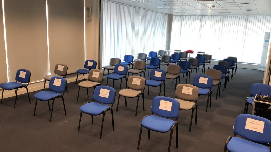 Aula vista desde la parte de delante con sillas de dos colores alineadas y separadas